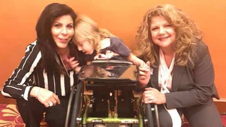 Angela Zervos and Lauren Calta posing with young girl in a wheelchair at the Shepherd Center Food and Supplies Fundraiser