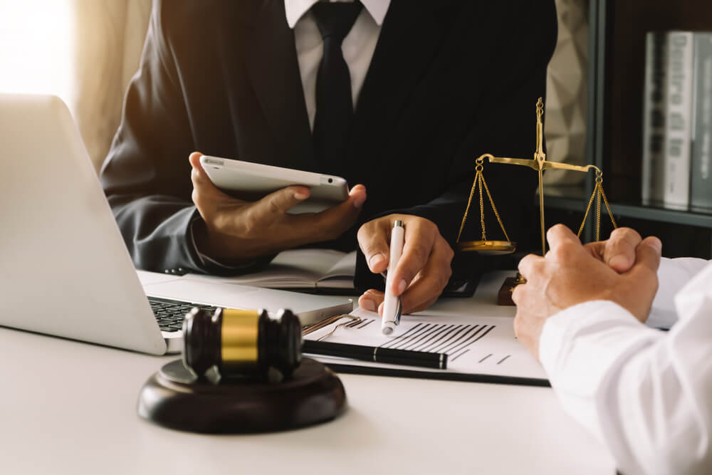 Two business professionals discussing legal documents related to personal injury cases in Florida, with a laptop, gavel, and scales of justice on the desk