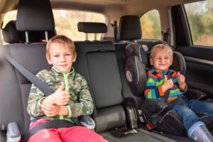 Two boys sitting on a car seat for safety.